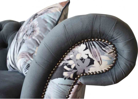 E e markant Dräisëtzer-Sofa am Chesterfield-Design mat delikaten groblommenden Dekoratioun.