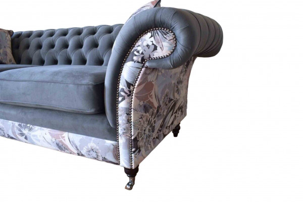E e markant Dräisëtzer-Sofa am Chesterfield-Design mat delikaten groblommenden Dekoratioun.