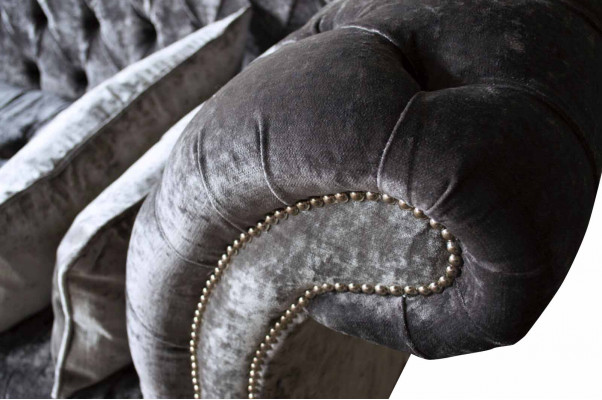 E bëqueemt, klassescht Sofa am Chesterfield-Stil an engem déif Sëlwertéin.