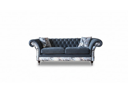 E e markant Dräisëtzer-Sofa am Chesterfield-Design mat delikaten groblommenden Dekoratioun.